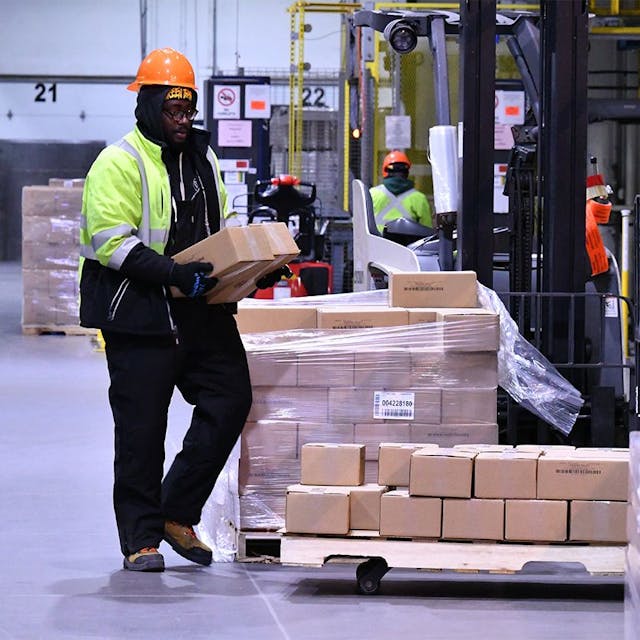 Man wearing hard hat carrying a box to load onto a pallet.