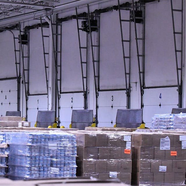 Cases of product in boxes on pallets in front of doors in a tall storage building.